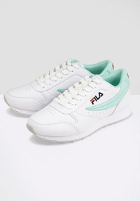 Baskets FILA blanches avec des accents vert menthe et des lacets blancs, montrées de côté sur une surface blanche.