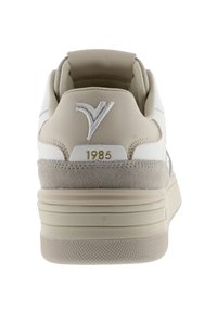 Sneaker beige e bianco con tallone in suede testurizzato, logo impressa e dettaglio dorato "1985". Presenta una suola stratificata con grip a mosaico.
