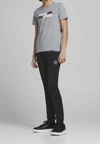 Graues Baumwoll-T-Shirt mit "JACK&JONES"-Logo in Marineblau und Bordeaux, kombiniert mit schwarzen Skinny-Hosen und schwarzen Sneakers mit weißen Sohlen.