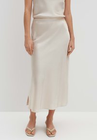 Jupe midi en satin crème avec une texture lisse, une fente sur le côté et une taille ajustée, associée à un haut assorti et des sandales de couleur claire.