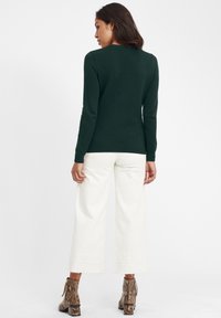 Tumed roheline koemustriga kootud sviiter, pika varrukaga ja ümar kaelus. Kombineeritud avara lõikega valgete pükste ja sisalikumustriga saapatega.