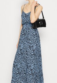 Maxi šaty v světle modré barvě s černými zebra pruhy, s přiléhavým korzetem, tenkými ramínky a splývavou sukní. Černá kabelka se čtvercovou sponou.