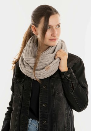 Lichtgrijze gebreide infinity-sjaal met een ribbelstructuur, gedragen over een zwarte denimjack. Aangekleed etiket zichtbaar op de sjaal.