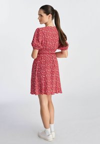 Czerwona sukienka w kwiaty z krótkimi bufiastymi rękawami, zgromadzonym w talii i zwiewnym dołem. Stylizowana z białymi tenisówkami i skarpetkami do kostek.