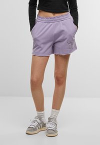 Pantaloni corti in pile lavanda con vita elasticizzata, tasche laterali e orli sfilacciati. Presentano un design ricamato sulla coscia sinistra.
