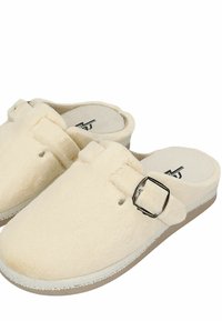 Crèmekleurige klompen met een zachte stoffen bovenkant, voorzien van een gespaccent, ronde neus en een textuurzool voor grip en comfort.