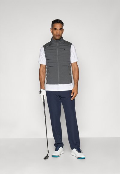 Graue Steppweste über einem weißen kurzärmeligen Hemd, mit blauen Hosen und weißen Golfschuhen. Hält einen Golfschläger, einfaches Design mit einem Reißverschluss vorne.