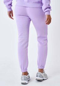 Lila joggerbroeken van zacht materiaal, met elastische boorden en een relaxed fit. Gecombineerd met zilverkleurige sneakers.