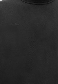 Κοντινή λήψη μαύρου υφάσματος που δείχνει διακριτικό ανάγλυφο κείμενο "COPENHAGEN" και ένα μινιμαλιστικό γεωμετρικό λογότυπο στην περιοχή του στήθους ενός πουκάμισου.