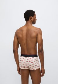 Ανδρικά μποξεράκια με ανοιχτό κρεμ χρώμα βάσης, διακοσμημένα με σχέδιο κόκκινα κεράσια, μαύρη ελαστική μέση με μικρή κόκκινη λεπτομέρεια.