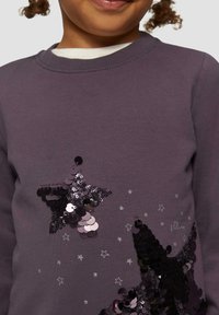 Paarse katoenen sweatshirt met stervormige ontwerpen van zwarte en zilveren pailletten, omringd door kleine zilveren sterren die om de pailletten zijn gedrukt.