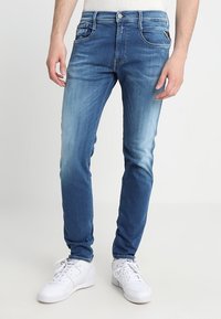 Slim-fit blå denimjeans med en urtvättad finish. Har fram- och bakfickor, bälteshällor och vita söm detaljer. Bärs med vita sneakers.