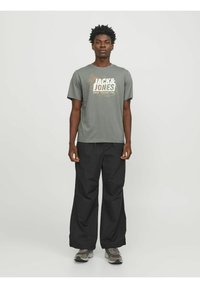 Camiseta gris con un estampado gráfico que dice "JACK & JONES", combinada con pantalones negros de corte holgado y zapatillas grises.