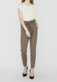 Beige hoge taille broek met een strikceintuur, met zijzakken, gecombineerd met een losse witte top met korte mouwen en zwarte hakken.