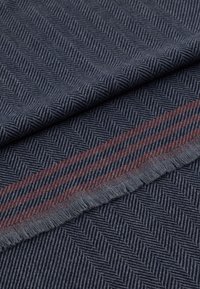 Temna tkanina z ribjo vzorcem v mornarsko modri in svetlo sivi barvi, z kontrastnim rdečim pasom ob robu.