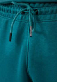 Teal trainingsbroek met een geribbelde tailleband, elastische koord en zwarte metalen uiteinden; zachte textuur en casual pasvorm.