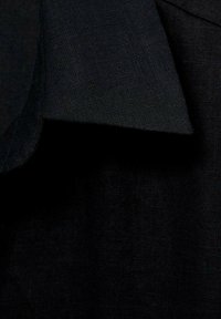Černá lněná tkanina s jemnou texturou, která má ohnutý okraj odhalující tkaní. Pozadí je v tmavší barvě, což zvyšuje kontrast.
