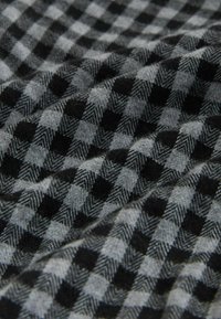 Țesătură tartan neagră și gri cu un model houndstooth, având o textură moale și dimensiuni variate ale pătratelor pe suprafață.