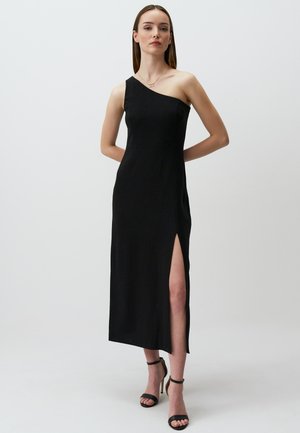Abito midi nero con una spalla sola e uno spacco laterale. Tessuto liscio e design aderente. Abbinato a tacchi a strappo neri. Semplice ed elegante.
