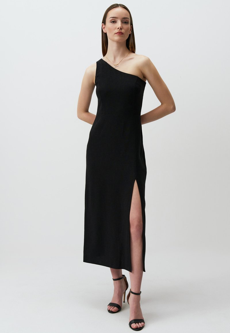 Abito midi nero con una spalla sola e uno spacco laterale. Tessuto liscio e design aderente. Abbinato a tacchi a strappo neri. Semplice ed elegante.