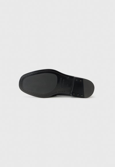 Black leather shoe sole with smooth texture, rounded shape, and small metal studs. Features contrast stitching near the heel.