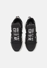 Juodi sportbačiai su tekstiliniu viršumi, su baltu spausdintu tekstu. Suapvalintas pirštas, storos raišteliai ir akcentuota pado dizainas.