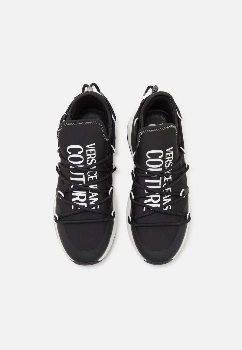 Schwarze Sneakers mit einem Obermaterial aus Textil, ausgestattet mit weißem Drucktext. Runde Zehenpartie, dicke Schnürsenkel und ein akzentuiertes Sohlen-Design.