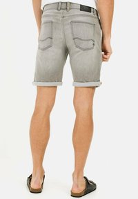 Graue Denim-Shorts mit umgeschlagenen Säumen, zwei Gesäßtaschen und einem Lederetikett am Bund, kombiniert mit schwarzen Sandalen.