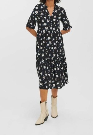 Woman wearing a black floral midi dress with half sleeves and cream pointed-toe ankle boots with block heels.