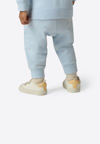 Light blue joggers with ribbed cuffs, paired with cream sneakers featuring a tan accent at the heel and light beige socks.