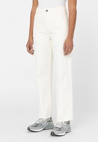 Witte katoenen broek met een rechte pasvorm, voorzien van zijzakken en een knoopsluiting bij de taille, gedragen met grijze en witte sneakers.