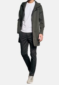 Długi oliwkowy zielony płaszcz, biały T-shirt, ciemne kraciaste spodnie i szare trampki. Płaszcz ma kaptur i zatrzaski.