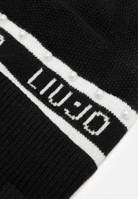 Berretto di maglia nero con fascia logo bianca, caratterizzato da perle lungo il bordo e texture a coste su tutto il corpo.