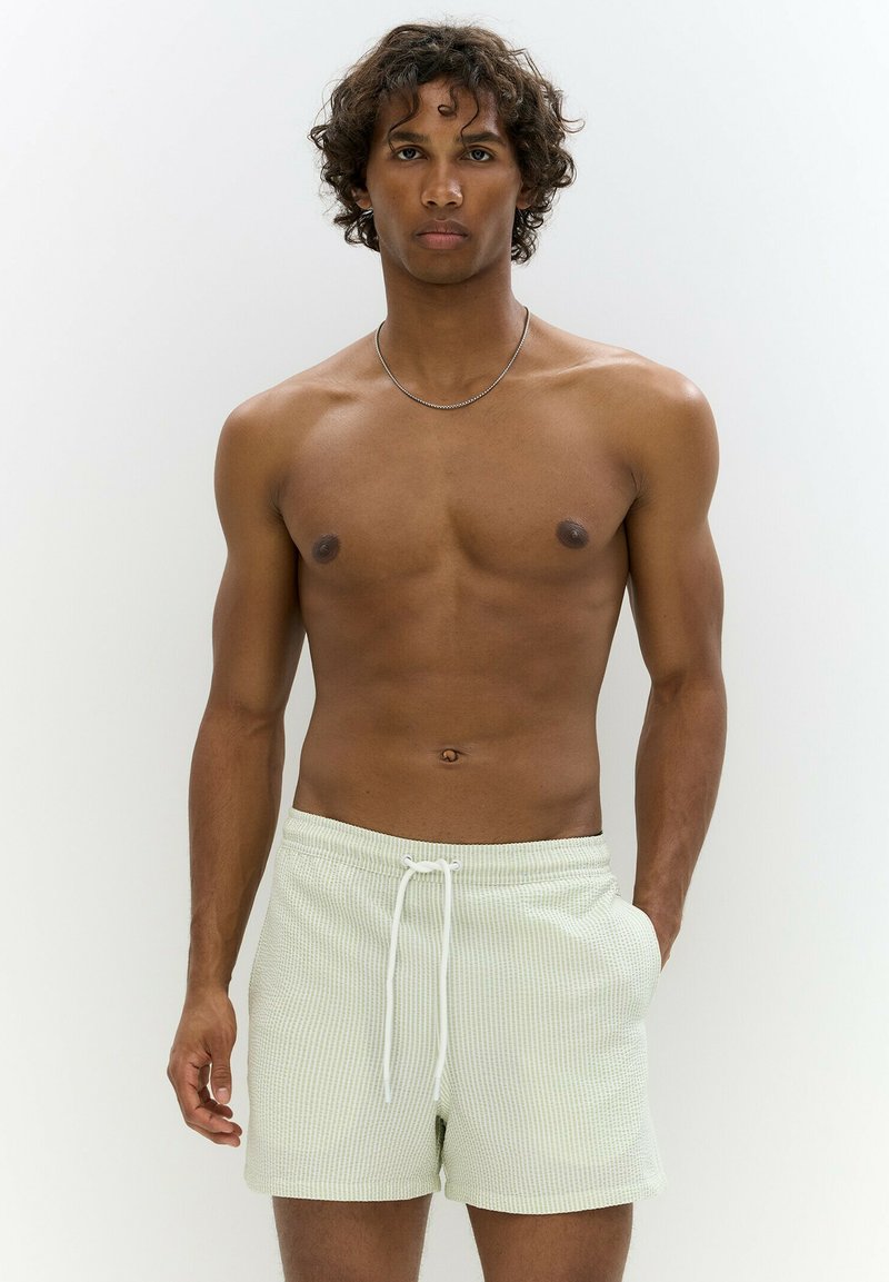 Világoszöld, bordázott rövidnadrág, húzózsinórral ellátott derékrésszel és oldal zsebekkel. Az anyag texturált megjelenésű. A modell semleges pózban van.