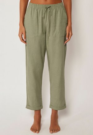 Olivegrüne Leinenhose mit elastischem Bund, vorderen aufgesetzten Taschen, Kordelzug und umgeschlagenen Säumen, barfuß getragen.