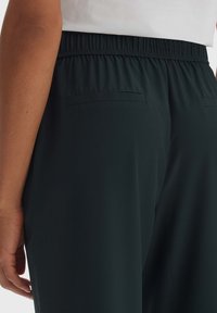 Dunkelgrüne Hose mit einem gerafften Gummibund, ausgestattet mit zwei kleinen Gesäßtaschen und einer glatten, leichten Textur.