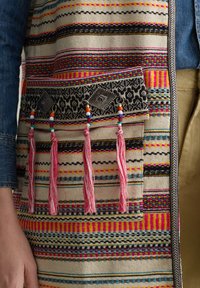 Multi-colored woven vest with geometric patterns, featuring a pocket decorated with tassels and beaded accents, primarily in pink and black.
