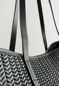 Schwarze Tragetasche mit gewobener Textur. Glatte Lederträger mit matter Oberfläche. Breite Öffnung und strukturierter Entwurf.