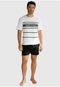 Weißes T-Shirt mit kurzen Ärmeln und schwarzen Streifen sowie "BRUNO BANANI" Logo; kombiniert mit schwarzen Shorts; schlichtes Design; entspannte Passform.