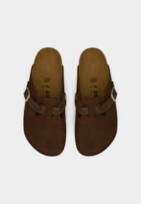 Καφέ παπούτσια τύπου clogs με σουέντ υφή, ρυθμιζόμενο καφέ λουράκι και στρογγυλή αγκράφα. Μαλακό ανατομικό πέλμα, μέγεθος 36, μινιμαλιστικός σχεδιασμός.