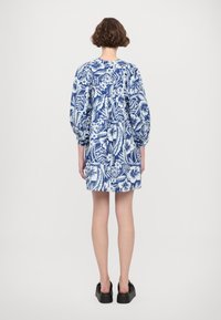 Bloemmotief jurk in blauw en wit, met opgezette mouwen en een achterkant plooi. Draagt met dikke zwarte platform schoenen.