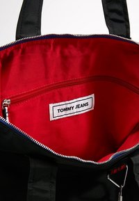 Borsa tote nera con interno rosso, dotata di chiusura con zip, piccola tasca interna e etichetta bianca con la scritta "TOMMY JEANS".