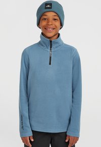Lyseblå fleecepullover med halvlukket krave, tekstureret stof og "Oneill"-branding. Bæres med en matchende blå strikhue.