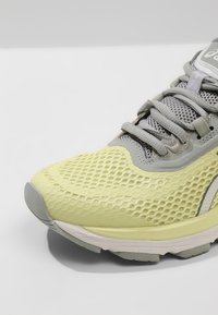 Baskets de course jaune clair avec une tige en mesh, accents gris, semelle texturée et lacets plats. Bout arrondi notable et amorti minimal.