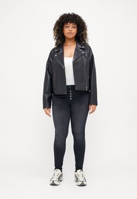 Black faux leather biker jacket, cropped design with asymmetrical zipper, paired with black jeans and white tank top, worn with sneakers.