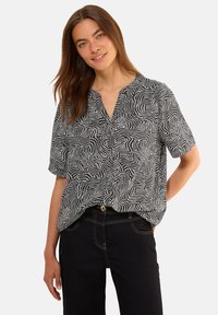 Blouse à manches courtes noir et blanc avec un motif en vagues, décolleté en V et coupe décontractée, accompagnée de jeans foncés.
