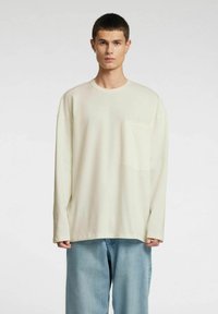 Langermet, kremfarget t-skjorte med rund hals og brystlomme; myk tekstur, avslappet passform, kombinert med lyseblå, vide jeans.