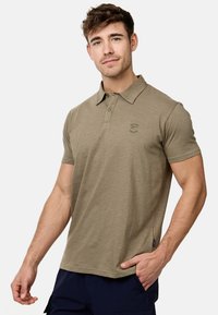 T-shirt polo vert olive en tissu doux, avec un col, des manches courtes et un petit logo sur la poitrine. Accents de couture et d'étiquette.