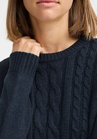 Dunkelmarineblaue Strickpullover mit Zopfmuster, gerippten Bündchen und Rundhalsausschnitt. Die Textur wirkt dick und warm.