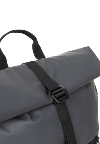 Zaino grigio con chiusura roll-top, realizzato in materiale impermeabile, con una tracolla nera e superfici texturizzate. Include una maniglia per il trasporto.